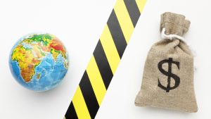 A globe and a burlap sack with a dollar sign are separated by a black and yellow caution tape, symbolizing economic barriers or financial restrictions in global markets.