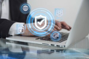 A businessman typing on a laptop with digital cybersecurity icons overlayed, including a shield with a checkmark, a globe, and data analytics, representing online security and data protection.